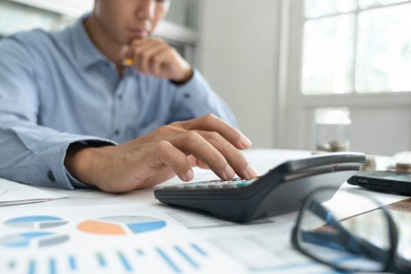 Portrait of young teacher with book smiling at camera while standing in the classroom and teaching at school